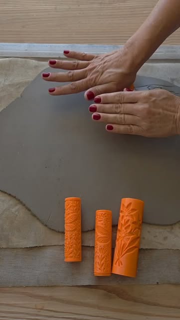 Mãos trabalhando uma placa de argila com ferramentas de textura sobre a mesa do ateliê